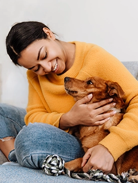 a woman sitting on a couch with her small brown dog 